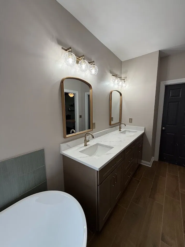 After: Bathroom remodel by CNB Renovations with new double vanity, gold mirrors, herringbone tile floor